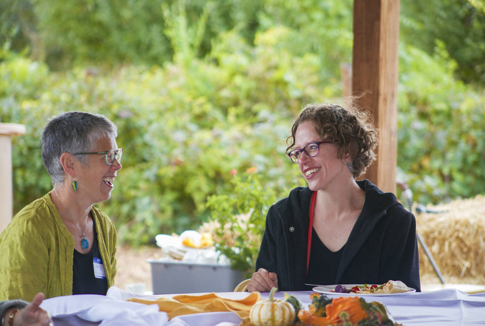 woman smiling at another woman across a table sitting outside