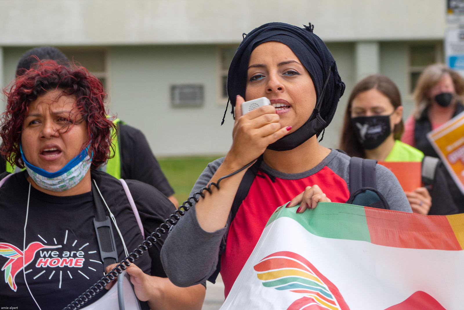 A woman in a hijab leads a march holding a banner and a bullhorn microphone