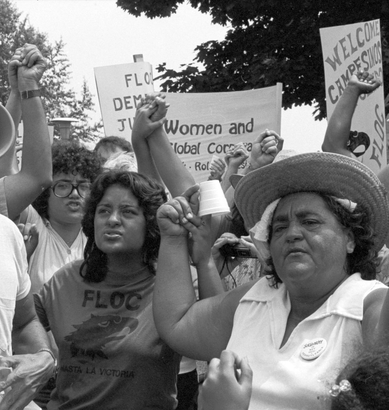 black and white archival photo of many different immigrant rights protestors holding up signs and raised fists. The signs say 