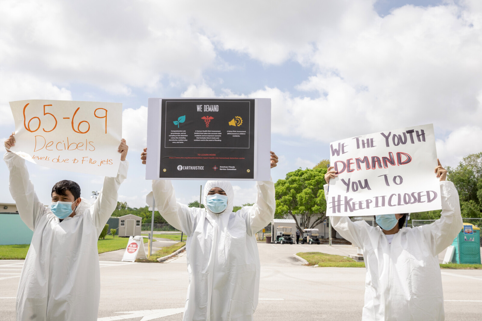 protesters in hazmat suits holding signs