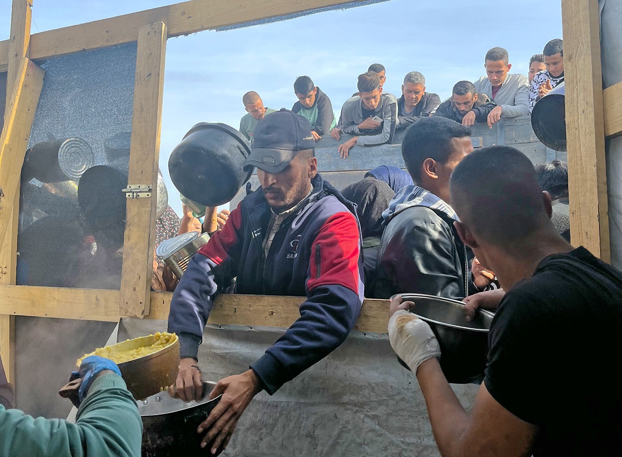 Man leans through window to accept a bowl of food. Many people are behind him. 