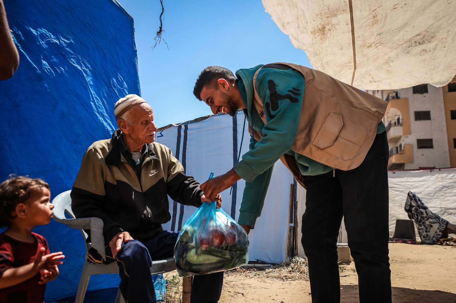 Man hands plastic bag of food to older man sitting down next to child