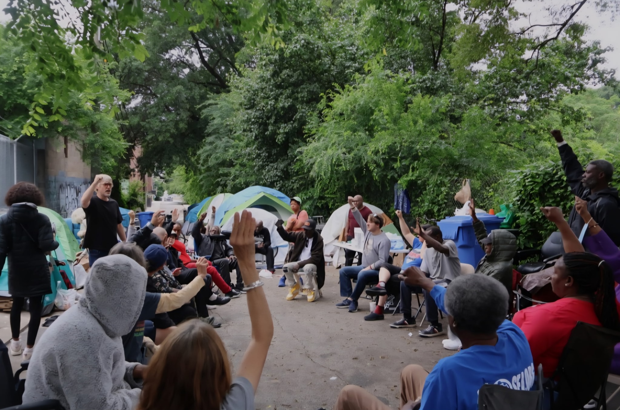People gather in a circle in front of tents outside