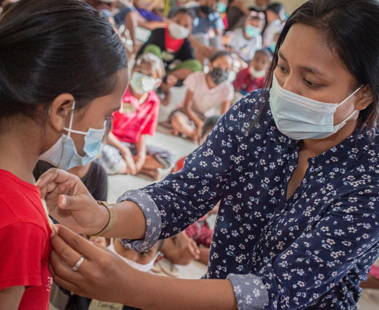 Woman affixing sticker to young girl's shirt.